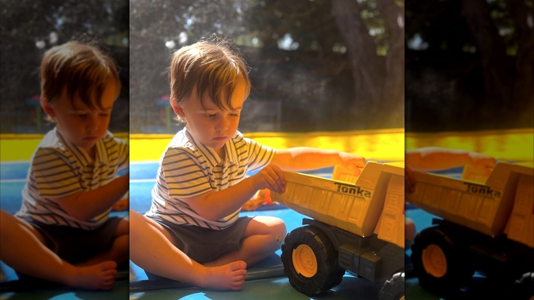 Katie Couric's grandson sitting cross-legged on the ground while playing with a Tonka truck