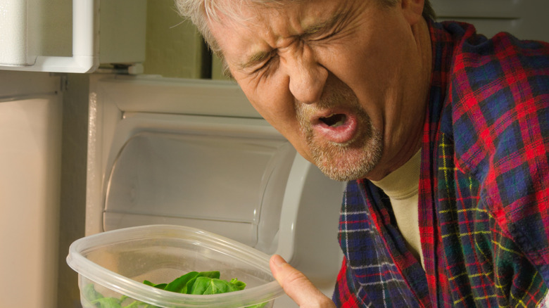 man showing disgust at leftover container he opened from refrigerator