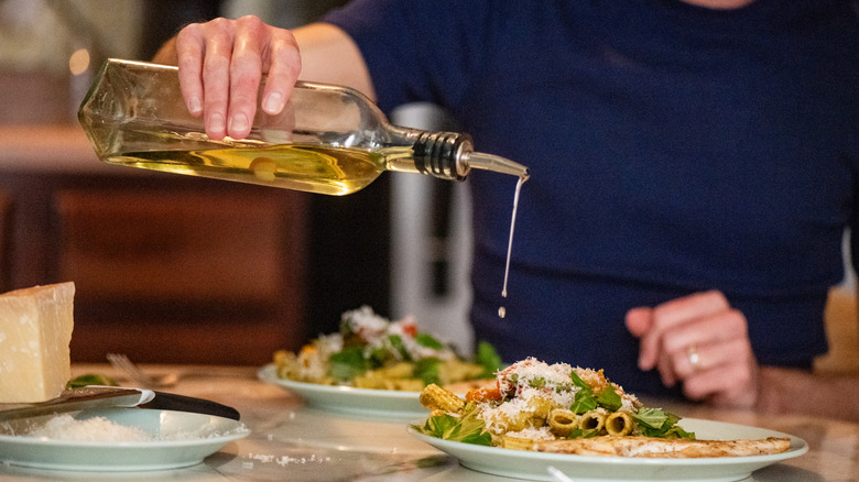 A man in pouring olive oil over his pasta.