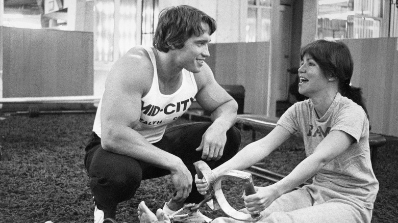 Bodybuilder Arnold Schwarzenegger training actress Sally Field on the rowing machine.