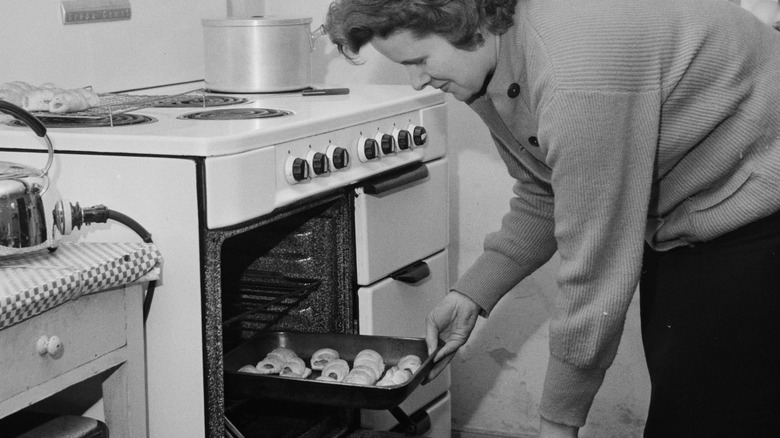 woman taking home cooked meal out of oven in 1950s kitchen