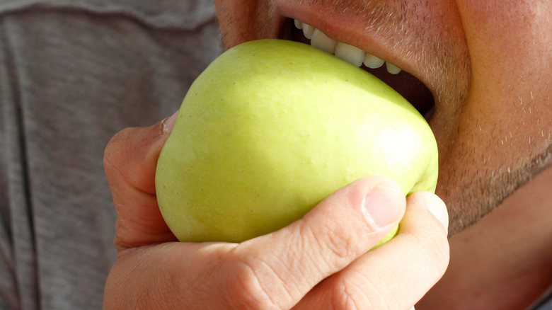 man's mouth biting into a green apple
