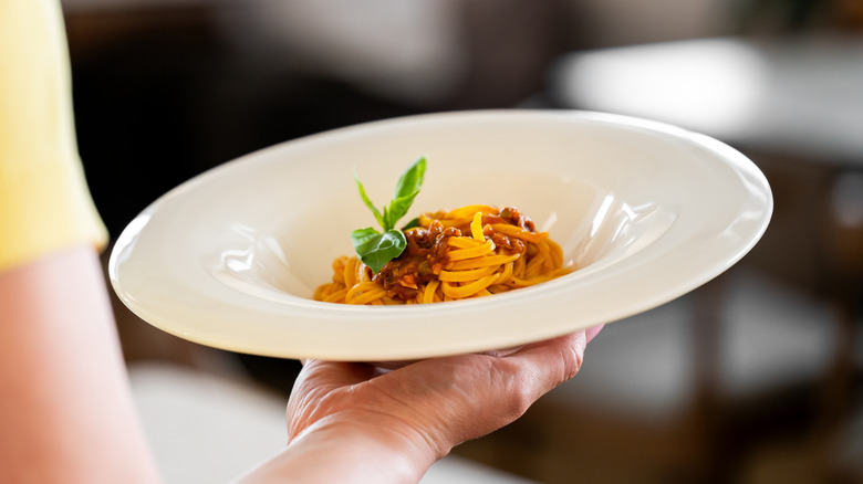 woman from behind holding small portion size of pasta on plate