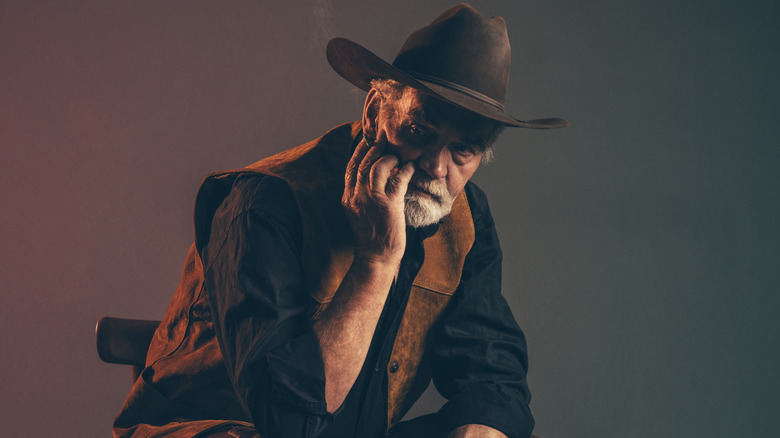older cowboy looking worn out while sitting on a small chair