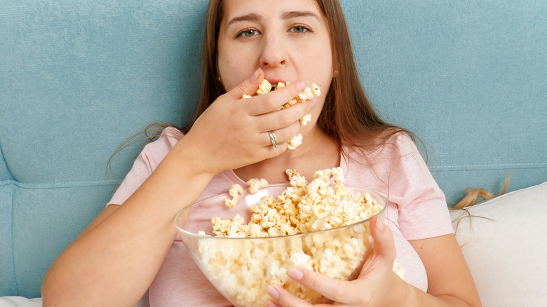 woman looking at camera and eating a handful of popcorn while in a resting position