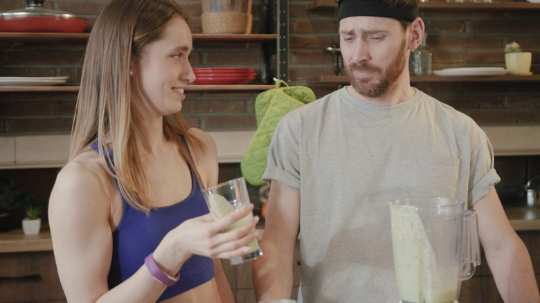 woman trying to get man wearing headband to like a blender shake