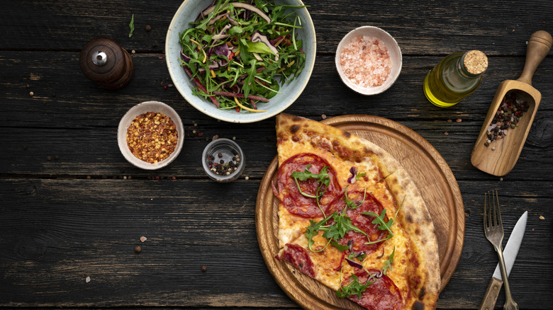 Pizza next to salad and other ingredients